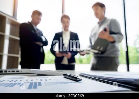 business document in touchpad lying on the desk, office workers discussting meeting in the background Stock Photo