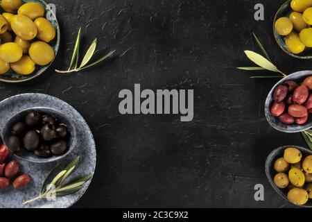 Olives, green, black and red, an assortment with leaves on a dark table with a place for text, a flat lay design template Stock Photo