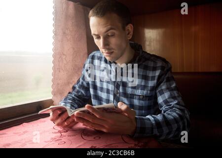 Young man sits at table in train read book. Travel concept Stock Photo