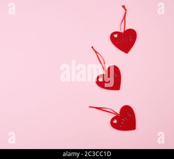 three felt red hearts on a pink background. Holiday celebration concept. Stock Photo
