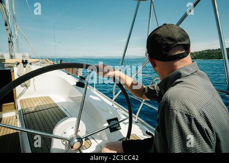 Male skipper on the steering wheel of a yacht. Sailing and yachting concept. Stock Photo