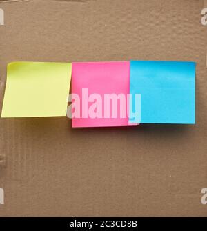 blank square multicolored sheets of paper stickers glued on a brown cardboard surface Stock Photo