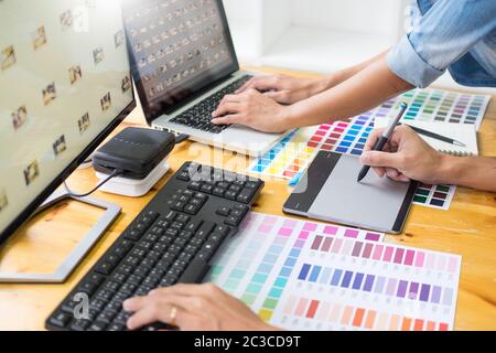 graphic designer team working on web design using color swatches editing artwork using tablet and a stylus At Desks In Busy Creative Office Stock Photo