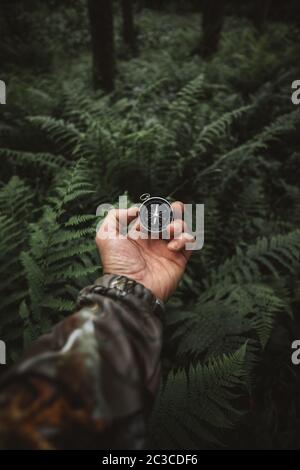 Survivor man searching the directions with a magnetic compass in the wilderness green forest Stock Photo