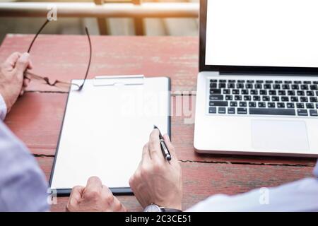 Two businessmen discussing planing tasks with laptop computer sitting at outdoor table. Stock Photo