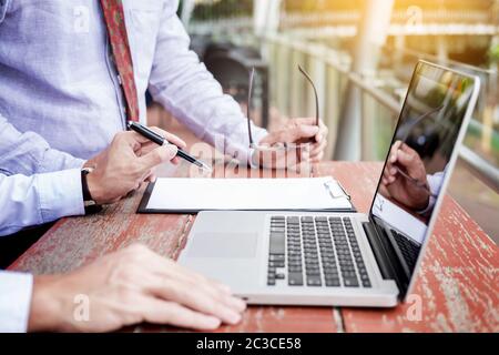 Two businessmen discussing planing tasks with laptop computer sitting at outdoor table. Stock Photo