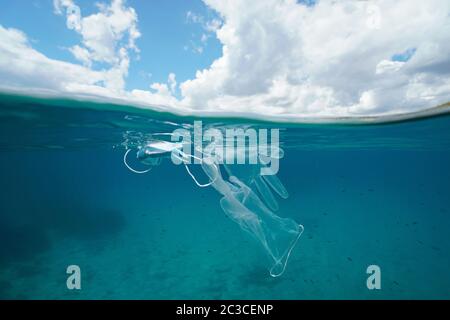 Plastic waste pollution in sea since coronavirus COVID-19 pandemic, face mask with gloves underwater and sky with cloud, split view over under water Stock Photo