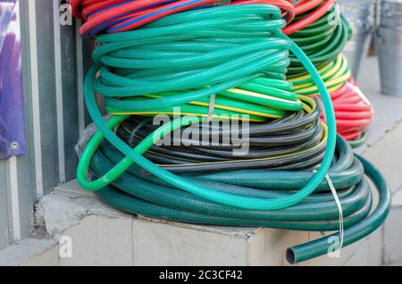 Stack of garden hoses. Variety of watering hoses stacked against the wall. Local market. Side view. Selective focus. Stock Photo