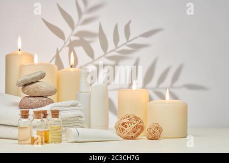 Spa still life with creams, essential oils, burning candles, stones and towels on light background with shadow from plant. Healthy lifestyle, body car Stock Photo