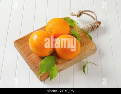 Three whole ripe oranges and leaves on cutting board Stock Photo
