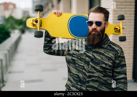 Urban guy lifestyle. Smiling bearded man with skateboard in extreme park. Subculture freedom. Stock Photo