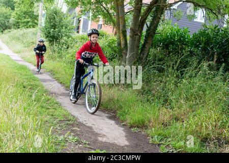 Two boys, one on a bicycle and one on a scooter, riding along a footpath Stock Photo