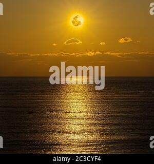 The moon and clouds in the golden sky above the ocean horizon at midnight, moonlight is reflected in the ribbed surface of the water. Night landscape, Stock Photo