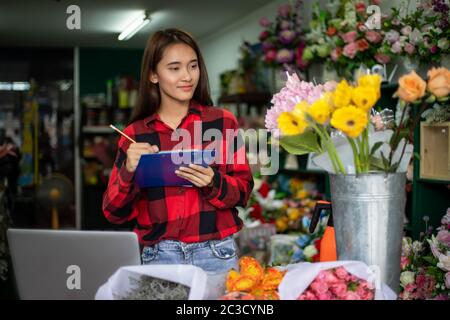 Asian Woman Florist Small Business Flower Shop Owner working and Holding A Clipboard  Writing to take orders for her store. Stock Photo