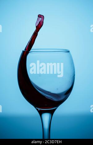 splashes of red wine in a glass on a black glossy glass on a blue background Stock Photo