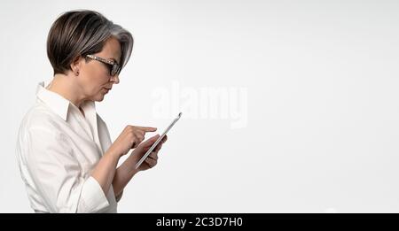 Gray-haired Caucasian businesswoman typing on tablet computer on white background. Horizontal template for ad banner with textspase at right Stock Photo