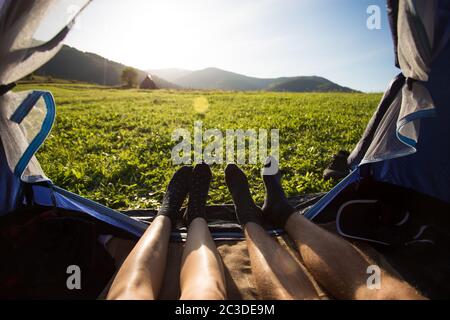 Two people lying in tent, view from inside. Couple camping with beautiful view of mountains sunset Stock Photo