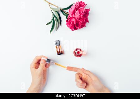 Overhead view woman's hands apply cosmetic serum next to bottle oil and flower on white background. Stock Photo