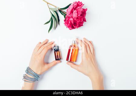 Top view female hands holding cosmetic serum and oil next to flower on white background. Stock Photo
