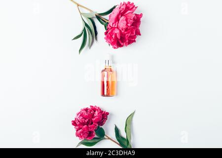 Beauty product cosmetic serum on white background next to fresh peony flowers, flat lay. Stock Photo