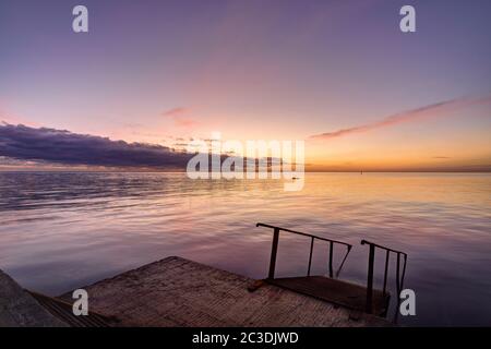 view of the evening sea from the pier, a ladder descends into the sea Stock Photo
