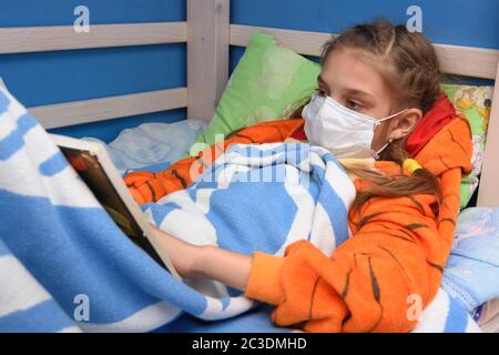 Sick girl in medical mask lies in bed and reads a book