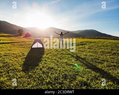 Aerial view of cheering woman near tent open arms at sunrise mountain peak wellness concept Stock Photo