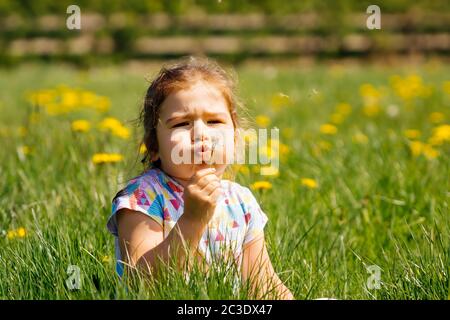 Young girl blowing dandelion on meadow, summer day, blurred background Stock Photo