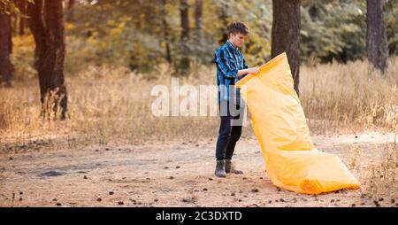 Autumn lifestyle of man inflates an inflatable orange sofa in forest. Relaxing and enjoying life on air bed banner format Stock Photo