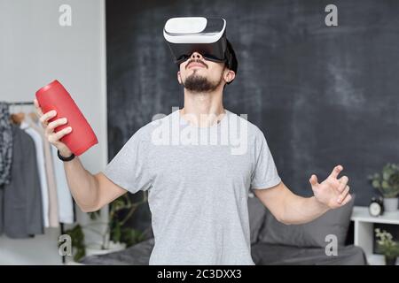 Young man in VR goggles holding portable speaker while exploring virtual world in video game Stock Photo