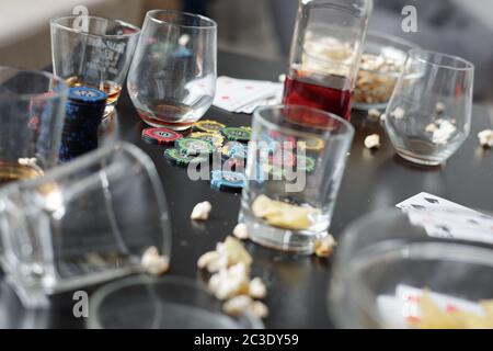 Close-up of empty dirty glasses, poker chips, playing cards and popcorn on table after poker party Stock Photo