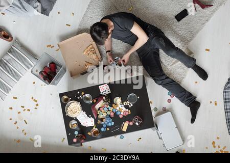 Above view of young man lying on floor and watching party photos after home party Stock Photo