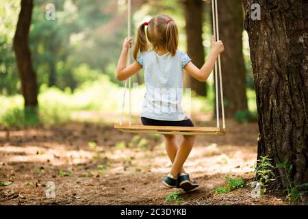 Happy Little girl on a swing in the summer park. Happy childhood without internet and electronic gadgets Stock Photo