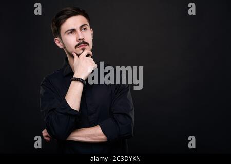 Pensive handsome young man in black shirt touching chin while brainstorming about idea Stock Photo