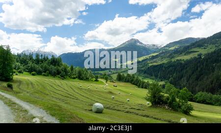 View of an alpine mountain landscape with farm fields and hay bales in the Swiss Alps above Andeer village Stock Photo