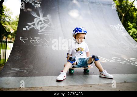 Boy with a skate in a skate park. The boy learns to skate, in full protection. Stock Photo