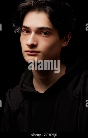 dramatic portrait of a young man in black clothes on a black background Stock Photo