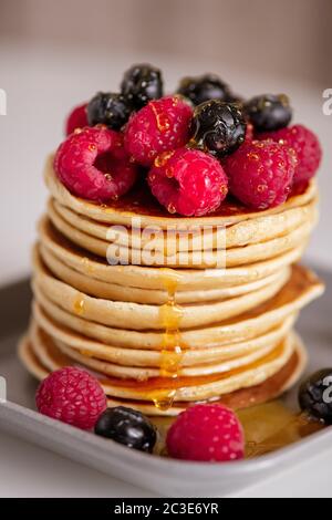 Pile of tasty ripe raspberries and blackberries and fresh honey on top of homemade pancake stack on grey plate cooked for breakfast Stock Photo