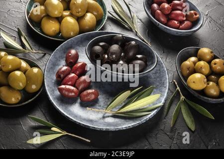 Olives, green, black and red, an assortment in bowls on a table Stock Photo