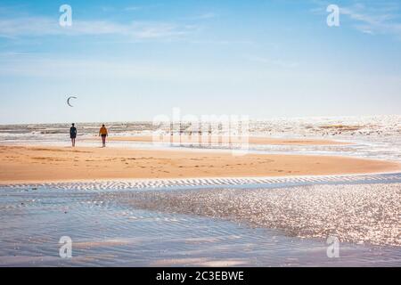 Two persons go for a walk on the wide sandy beach when the weather is nice Stock Photo
