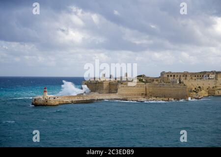 VALLETTA, MALTA - DEC 31st, 2019: View from Fort St Elmo on to the Ricasoli Grand Harbour East Breakwater and red lighthouse during strong waves Stock Photo