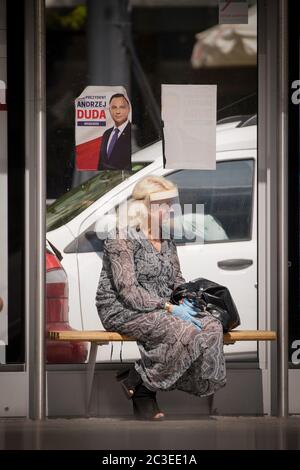 Warsaw, Poland. 19th June, 2020. A woman wearing a face shield is seen beneath a poster of incumbent Polish President Andrzej Duda at a bus stop in Warsaw, Poland, on June 19, 2020. Poland will hold its presidential elections on June 28, with a run-off round two weeks later. The elections, which were originally scheduled for May 10, did not take place due to the COVID-19 pandemic and the resulting lockdown. Credit: Jaap Arriens/Xinhua/Alamy Live News Stock Photo