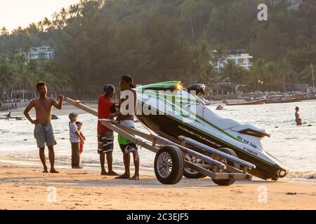 Phuket, Thailand - February 02, 2019: Mens at sunset pull jet ski out of the water on a sandy beach. Summer vacation. Water bike loaded onto a trailer Stock Photo