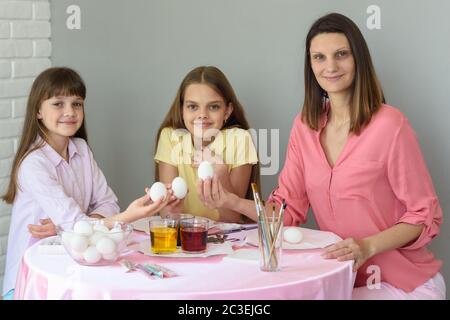 Mom and two daughters are sitting at the table preparing eggs for Easter and looked in the frame Stock Photo