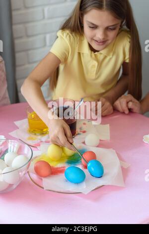Girl paints Easter eggs in a special solution and puts on a plate Stock Photo