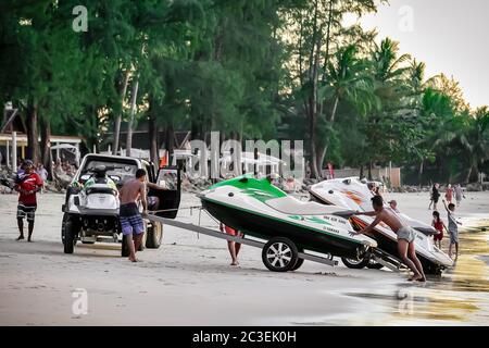 Phuket, Thailand - February 02, 2019: Mens at sunset pull jet ski out of the water on a sandy beach. Summer vacation. Water bike loaded onto a trailer Stock Photo