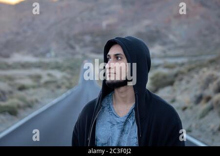 Tenerife, Spain - 12/19/17: A bearded man wearing a black hoodie and looking off into the distance on a long straight road Stock Photo