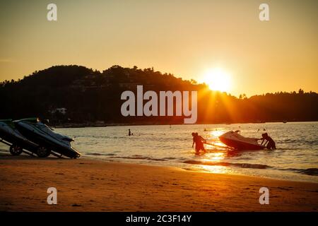 Phuket, Thailand - February 02, 2019: Mens at sunset pull jet ski out of the water on a sandy beach. Summer vacation. Water bike loaded onto a trailer Stock Photo