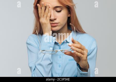 Portrait of young caucasian woman with glasses holding in hand rubbing her eyes, feels tired after working on laptop, focus on glasses. Overwork, tire Stock Photo