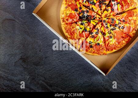 Pepperoni pizza with black olives in cardboard box on dark background. Stock Photo